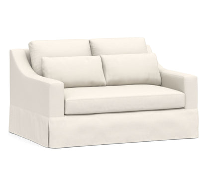 The York Slope Arm Deep Slipcovered Sofa is a cream-colored, plush loveseat featuring two large seat cushions and two back cushions. It comes with a tailored skirt and slightly curved armrests, providing a comfortable and elegant seating option.