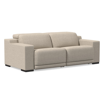 The Dalton Motion Sofa is a sleek and modern piece featuring a beige upholstery, wide armrests, and two large seat cushions. It rests elegantly on short, dark legs.