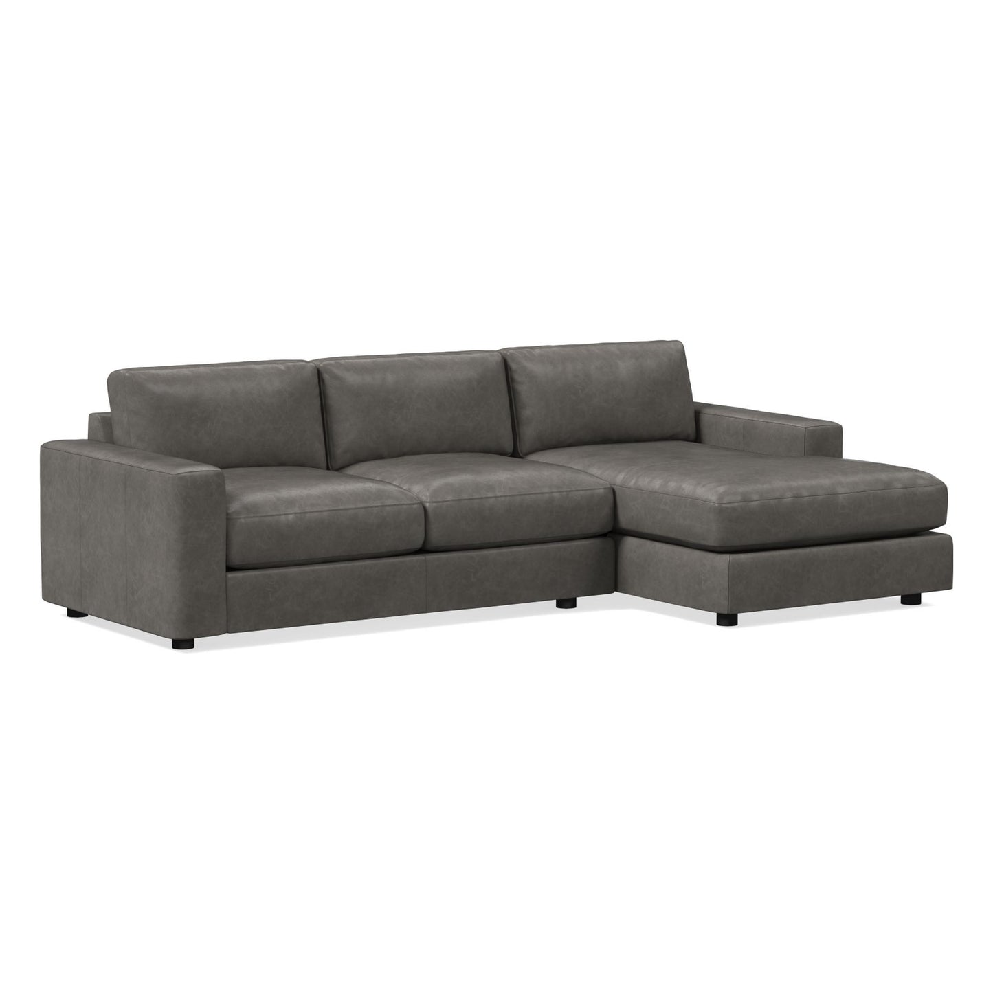 Introducing the Urban Leather 2 Piece Chaise Sectional, a modern dark gray sofa that features three cushion seats and an extended chaise on the right side. It boasts a minimalist design with sturdy black legs, making it ideal for a contemporary living room setting.