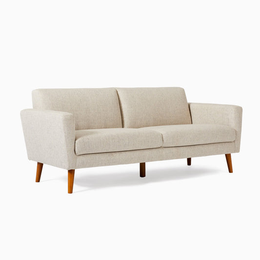 The Oliver Sofa is a beige mid-century modern piece featuring wooden legs. It boasts two seat cushions and a minimalist design, elegantly displayed against a plain white background.