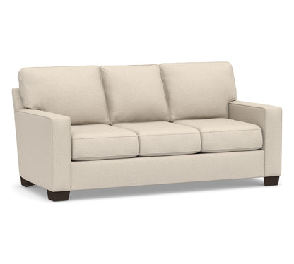 The Buchanan Square Arm Sleeper Sofa is a beige, three-seater sofa featuring square arms and dark wooden legs. Its plush cushions are neatly aligned, providing a comfortable and modern appearance. The plain white background effectively highlights the design of the sofa.