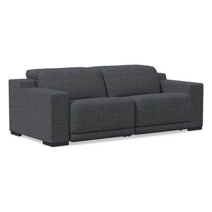 The Dalton Motion Sofa is a modern piece in dark gray, featuring wide armrests and thick cushions set against a white background. It boasts a minimalist design with a boxy shape and low profile.