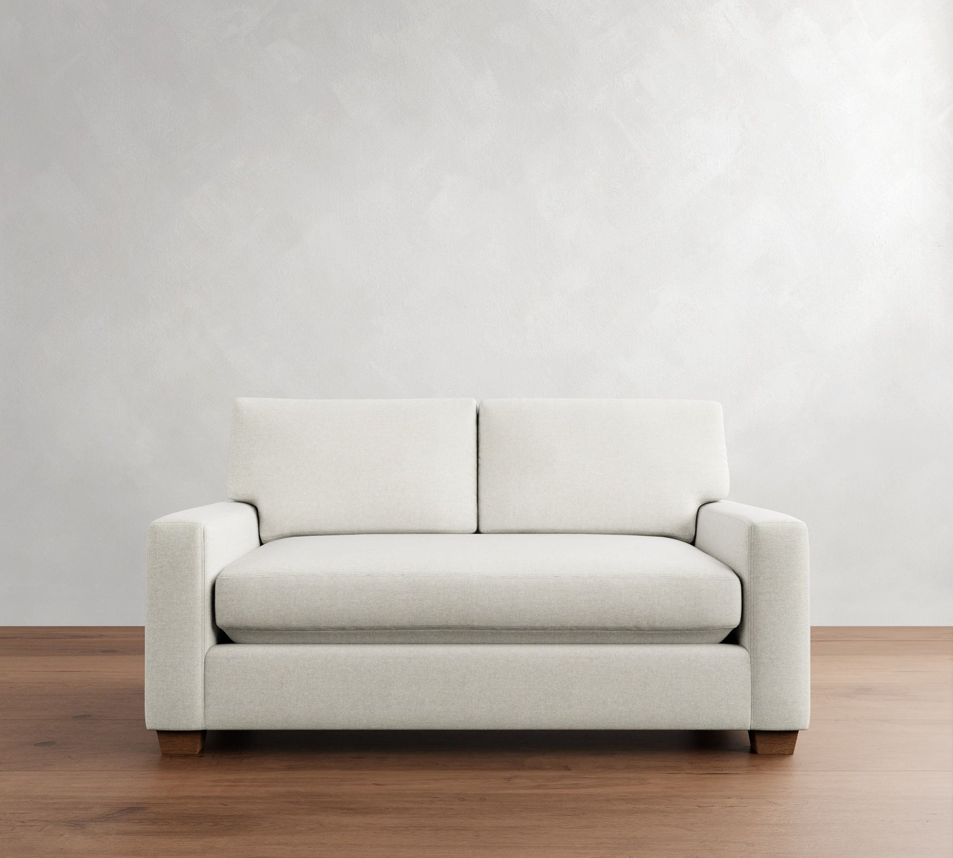 A PB Comfort Modern Square Arm Upholstered Sofa, with its minimalist design and two seat cushions, sits on a wooden floor against a light gray wall, showcasing its simple, clean lines and sturdy base.