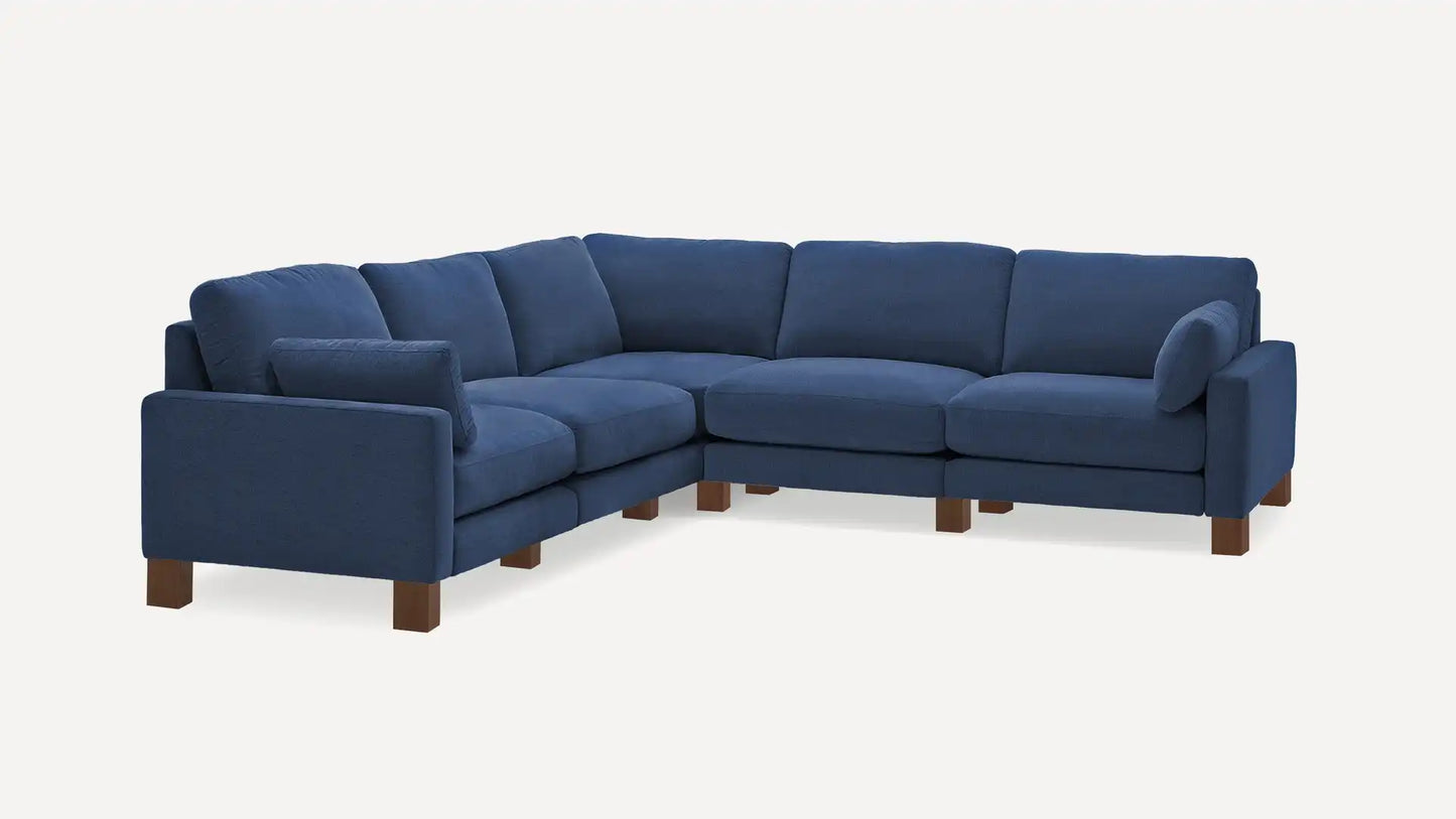 The Union Fabric Modular 5-Seat Sofa Sectional is a blue, L-shaped sectional sofa featuring cushioned seats and backrests. It boasts a modern design with wooden legs, elegantly set against a plain white background.