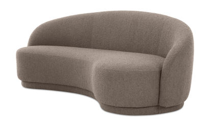 The Excelsior Sofa Cream is a modern loveseat in light brown, featuring a curved back and plush fabric. Its distinctive, rounded design with no visible legs offers a minimalist and cozy look.