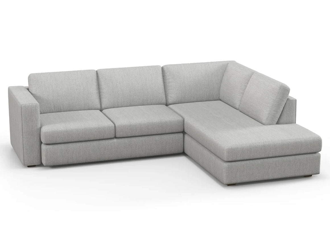 The Lounge Bumper Sectional is a light gray L-shaped sofa that includes three seat cushions, three back cushions, and features a chaise on the right side. It boasts a modern, minimalist design and is displayed against a plain white background.