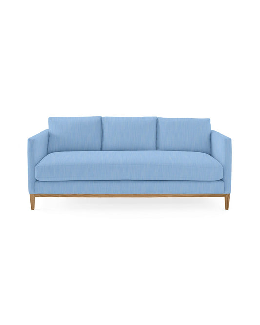 A contemporary Barton Sofa in a light blue hue featuring three back cushions and wooden legs, showcasing a sleek, minimalist design against a plain white background.