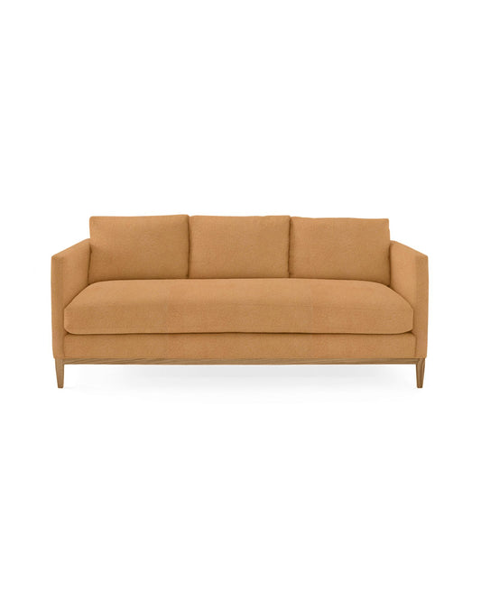 The Barton Sofa is a contemporary piece featuring a mustard color, three plush cushions, and sleek wooden legs set against a plain white background.