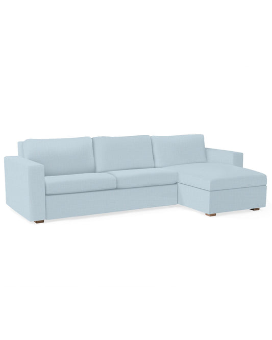 The Conover Sleeper Chaise Sectional features a light blue color with three seat cushions and an extended chaise on the right side, set against a white background. It boasts block arms and wooden legs, providing a modern and minimalist design.