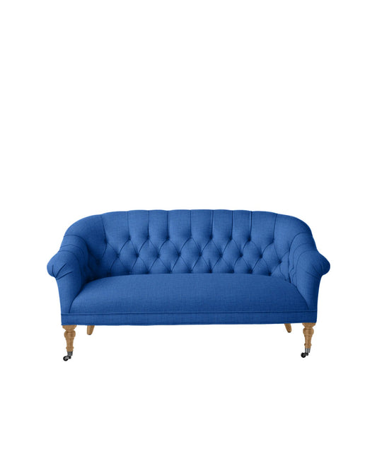 The Paxton Tufted Loveseat in blue, featuring wooden legs, a tufted backrest, and cushioned armrests, is showcased against a white background.