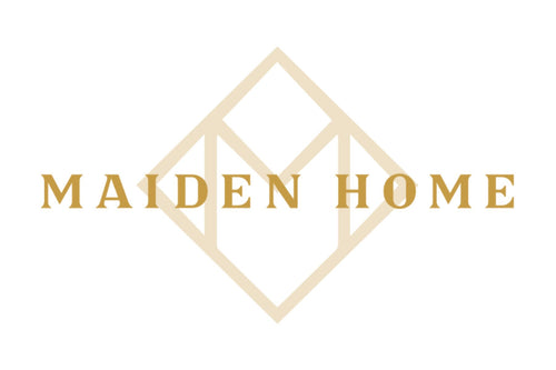 The image displays the logo for Maiden Home. It features the text "MAIDEN HOME" in gold capital letters, with a geometric, diamond-shaped design in the background. The design includes an abstract letter "M" integrated into the diamond shape.