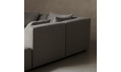 The Breuer Modular Chaise Armless Sectional 114" in Belgian Linen Agate, a minimalist and modern gray sofa with clean lines and multiple matching cushions, sits against a simple, neutral-toned background. The focus is on the back and side views of this elegant furniture piece.