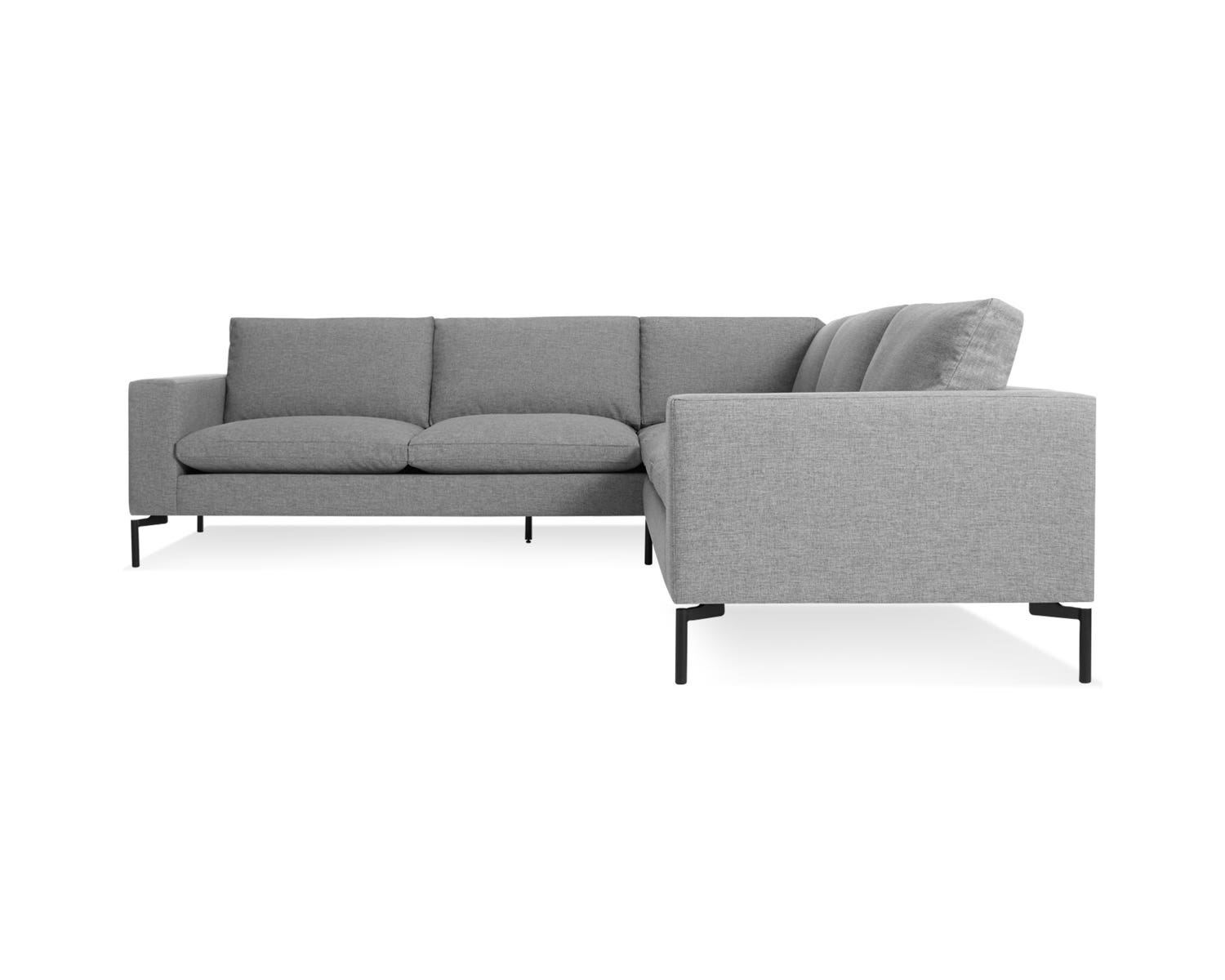 A side view of the New Standard Sectional Sofa showcases its modern design with gray upholstery, clean lines, and sleek black legs. The smooth fabric and plush cushions promise a comfortable seating experience against a plain white background.