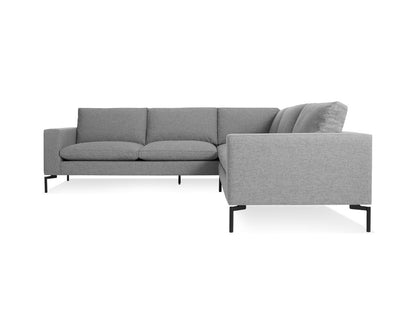 A side view of the New Standard Sectional Sofa showcases its modern design with gray upholstery, clean lines, and sleek black legs. The smooth fabric and plush cushions promise a comfortable seating experience against a plain white background.