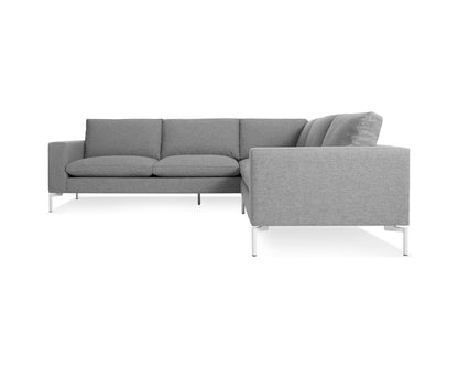 Introducing the New Standard Sofa Sectional: a gray L-shaped sectional with a modern design. It includes three seat cushions and a comfortable backrest, all supported by sleek white metal legs. Presented on a plain white background, this sofa highlights its simple and contemporary style.