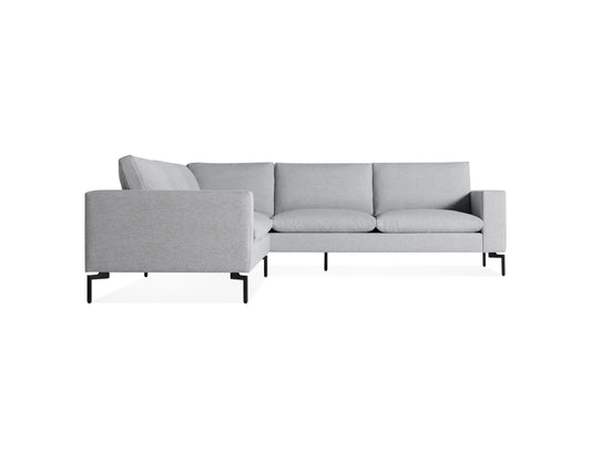 The New Standard Sofa Sectional presents a minimalist and modern look against a white background, featuring a light gray L-shaped design with slim black metal legs, three seat cushions, and matching back cushions.