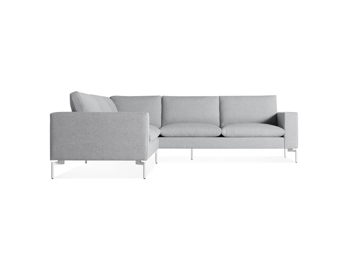 The New Standard Sofa Sectional features a light gray L-shaped design with clean lines and a minimalist aesthetic. It is equipped with cushioned backrests and seat cushions, supported by slender metal legs, offering a modern and sleek appearance.