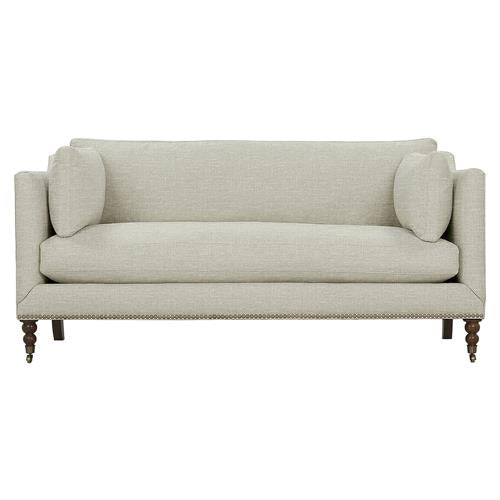 The Madeline French Grey Upholstered Sofa is designed with a smooth upholstery in a light beige tone and comes with two side pillows. Its rectangular backrest and wooden legs complement its simple yet elegant design, while brass casters and nailhead trim add subtle sophistication.