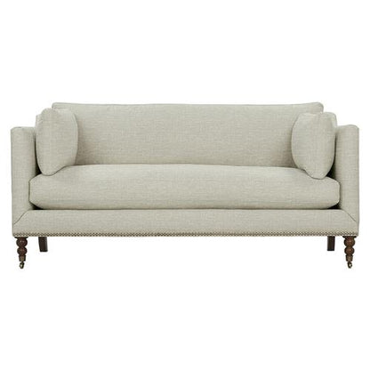 The Madeline French Grey Upholstered Sofa is designed with a smooth upholstery in a light beige tone and comes with two side pillows. Its rectangular backrest and wooden legs complement its simple yet elegant design, while brass casters and nailhead trim add subtle sophistication.