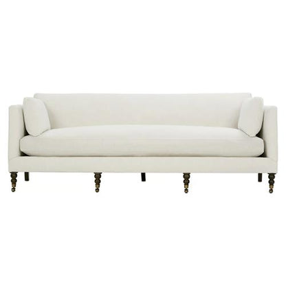 The Madeline French Grey Upholstered Sofa boasts a minimalist design with streamlined features, including soft cushions and slender, turned wooden legs. With its modern aesthetic accented by brass casters and nailhead details, this large sofa offers a chic seating option.