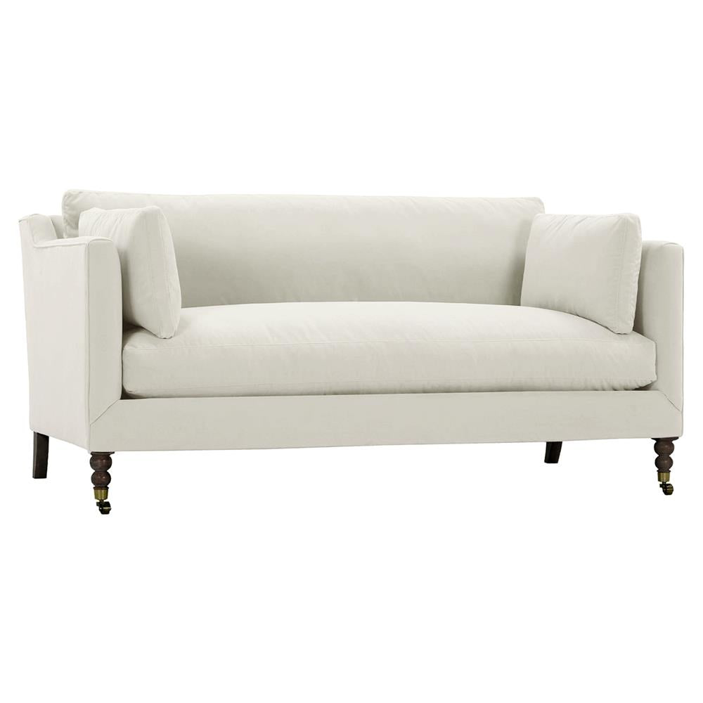 Introducing the Madeline French Grey Upholstered Sofa: a large, modern piece with plush seat cushions and a high backrest, adorned with two side pillows. The sofa features dark brown wooden legs with brass casters on the front for added mobility, complemented by decorative nailhead trim for a streamlined design.