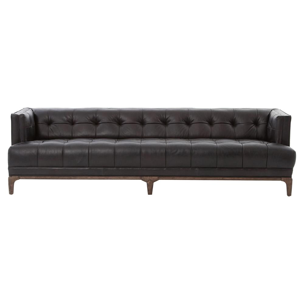 A mid-century sofa characterized by its green velvet upholstery and button-tufted design, featuring a brown wood frame and legs. This low-back piece includes armrests and offers a classic, elegant look perfect for a living room or office setting.