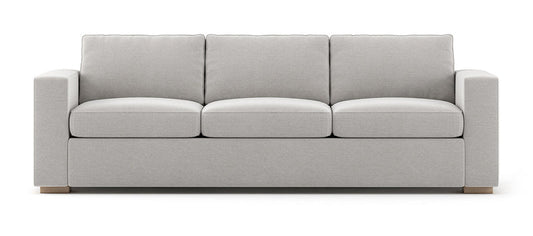 The Rio Sofa is a light gray three-seater with plush cushions and wide armrests, set against a white background with simple, modern design elements.