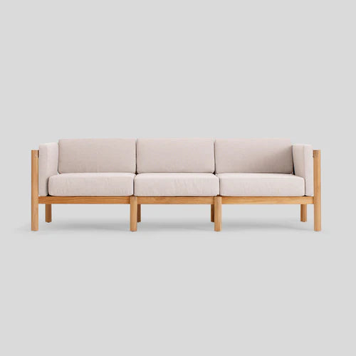 The Haven Sofa is a contemporary three-seater featuring light beige cushions and a wooden frame, displayed against a plain gray background.