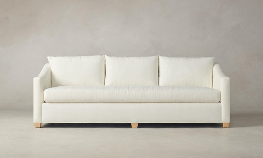 The Sullivan 60" Sofa in Performance Linen Weave, featuring three plush cushions and light wooden legs, is set against a neutral background. Its clean and modern design emphasizes comfort and simplicity.