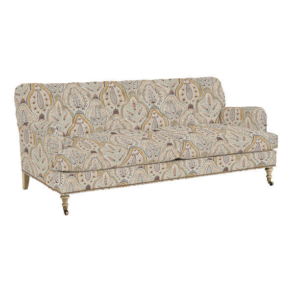 The Maggie Sofa with Brass Nailheads features a light-colored upholstery in a patterned paisley design. It boasts a traditional style with rolled arms and turned wooden legs on casters.