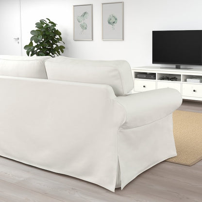 The living room features an UPPLAND Sofa positioned opposite a flat-screen TV resting on a sleek white console. Two framed botanical prints adorn the wall, while a green plant adds a touch of nature in the corner. The space is finished with light wood flooring and a beige rug, creating minimalistic decor.