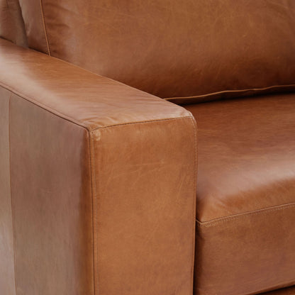 Close-up of the modern Urban Leather 2 Piece Chaise Sectional, focusing on the armrest and seat cushion to showcase the smooth texture and stitching details of its brown leather upholstery.