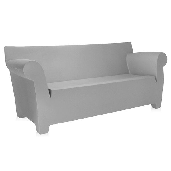 The Bubble Club Sofa by Kartell, featuring a minimalist gray design with curved armrests and a high backrest, is elegantly displayed against a plain white background. Its modern aesthetic is highlighted by clean lines and smooth surfaces.