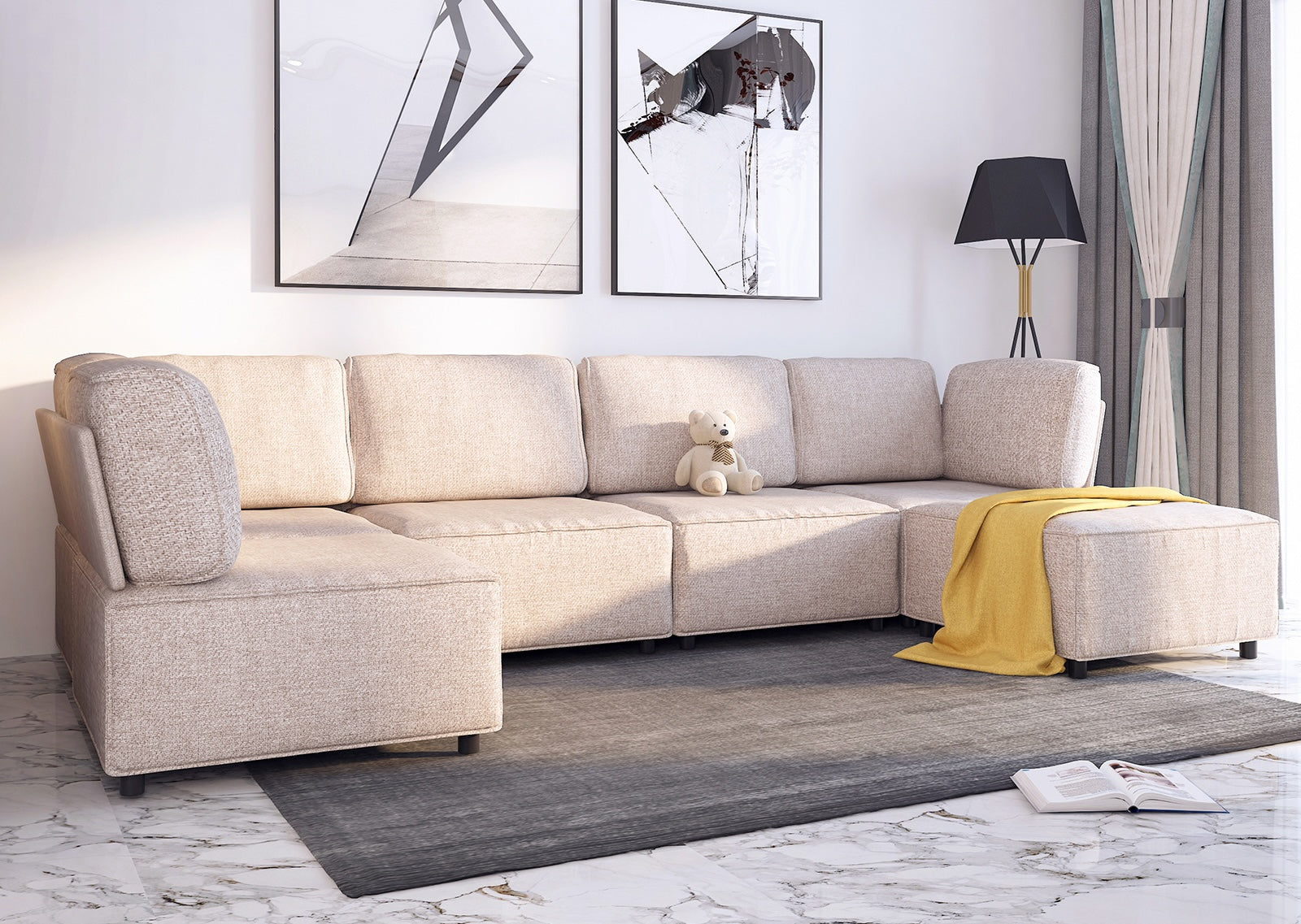 A modern living room features a beige sectional sofa with a yellow throw blanket and a stuffed teddy bear on one cushion. Two abstract art frames hang on the wall above the sofa. A black floor lamp stands next to the sofa, and an open book lies on the gray rug.