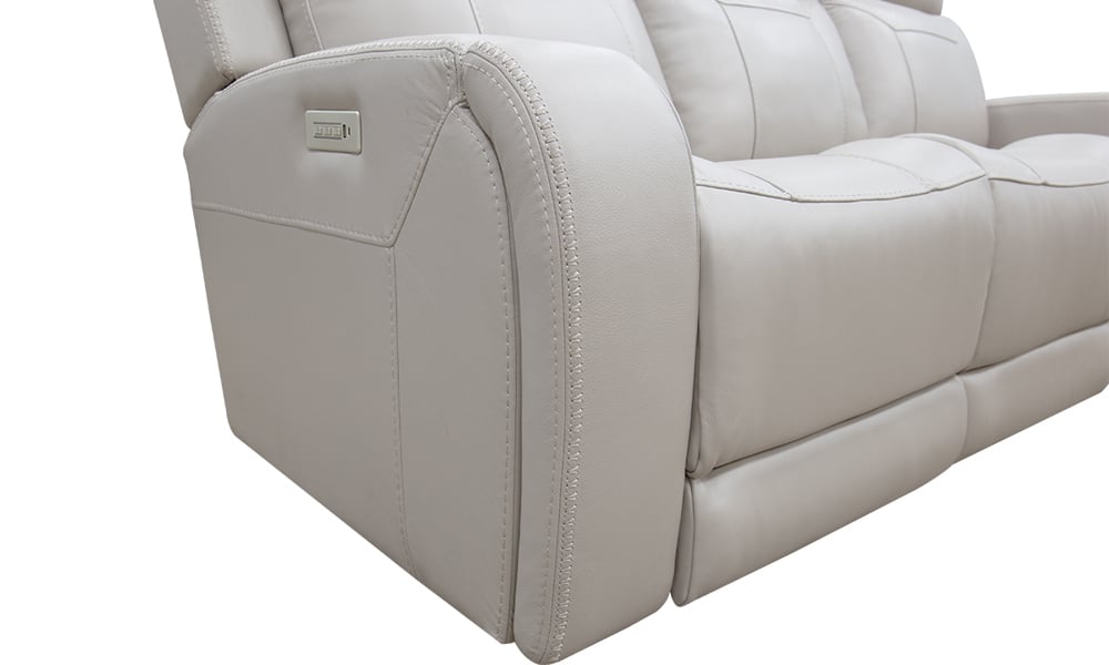 Close-up of the Maverick Dove Leather Power Media Sofa in light gray, featuring visible stitching details. The left armrest includes a control panel for adjusting the recline. The sofa showcases a smooth, modern design against a plain background.