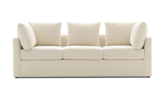 The Mitchell Gold + Bob Williams Dr Pitt Sofa is a modern, cream-colored, plush three-seater with clean lines and five matching cushions. Its minimalist design not only looks comfortable but also makes it ideal for a contemporary living room setting.