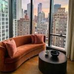 Cococozy lifestyle and home decor and interior design blog. Curved orange velvet upholstered couch with round black coffee table overlooking a dense downtown city at sunset.