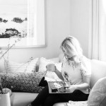 Jacquelyn Clark lifestyle and home decor and interior design blog. Black and white photo of a young woman reading a magazine with a cup of coffee. Black and white photography on the wall. Chunky toss pillows. White two piece sectional sofa.