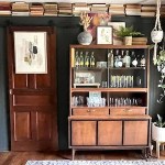 Jennifer Rizzo lifestyle and home decor and interior design blog. Dining room with large wooden bar hutch. Vintage glass barware, open shelves with old books, rope crochet plant holder, plant stand, modern art.