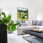 Maison de Pax lifestyle and home decor and interior design blog. Light and airy white living room. 2 piece sectional gray couch with blue and patterned toss pillows. Leather upholstered and diamond tufted coffee table with bronze legs. Country style impressionist painting.
